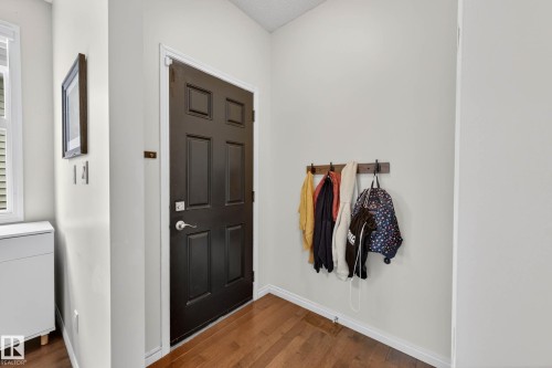 Entryway featuring a dark paneled door, wood-finish flooring, a window with horizontal blinds, a wall-mounted coat rack, and light-toned wall paint - 2007 72 Street, Edmonton, AB - Indoor Photo Showing Other Room