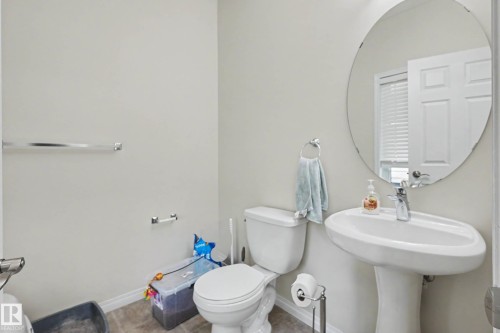 Powder room featuring a pedestal sink with a single-handle faucet, a circular mirror, and tile flooring - 2007 72 Street, Edmonton, AB - Indoor Photo Showing Bathroom