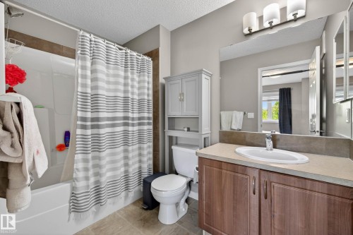 Full bathroom featuring a white tub-shower combination with brown tile surround, a single vanity with wood-finish cabinetry, a light-toned countertop with an integrated sink, and a large wall-mounted mirror - 2007 72 Street, Edmonton, AB - Indoor Photo Showing Bathroom