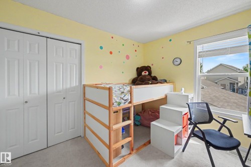 Bedroom featuring light yellow walls, white bi-fold closet doors, carpet flooring, and a white-framed window - 2007 72 Street, Edmonton, AB - Indoor