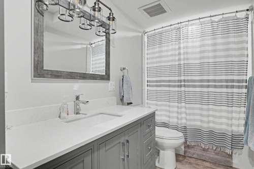 Bathroom featuring a gray vanity with a white countertop and integrated sink, chrome faucet, and a large mirror with a gray wood-look frame - 2007 72 Street, Edmonton, AB - Indoor Photo Showing Bathroom