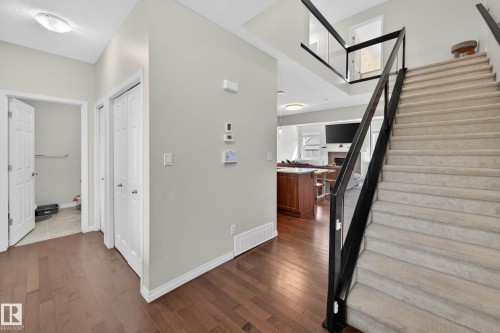 Entryway featuring wood-finish flooring, a carpeted staircase with a modern black and glass railing, and white trim - 2007 72 Street, Edmonton, AB - Indoor Photo Showing Other Room