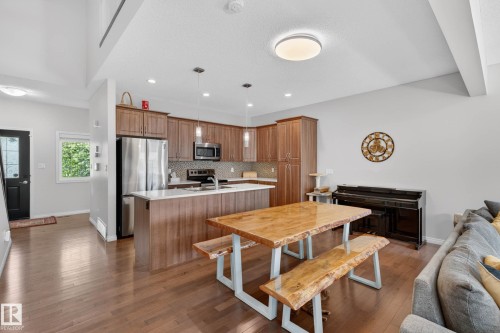 Open-concept living space featuring wood-finish flooring, a kitchen with stainless steel appliances, a center island with pendant lighting, wood cabinetry, and a mosaic tile backsplash - 2007 72 Street, Edmonton, AB - Indoor Photo Showing Kitchen