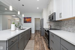 Modern kitchen featuring a large island with sink, white countertops, stainless steel appliances, and wood-finish flooring - 