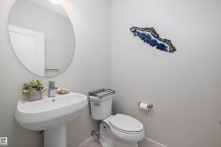 Pedestal sink with chrome faucet, complemented by a round wall mirror, and a white toilet - 