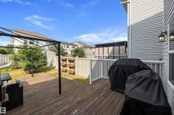 Expansive multi-level wood deck with white railings, featuring a gazebo structure, outdoor wall sconce, and a fenced backyard - 