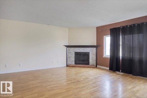 Spacious room featuring wood-finish flooring, a fireplace with a stone surround and dark wood mantel, and large windows - 13224 37 Street, Edmonton, AB 