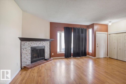 Living area featuring wood-finish flooring and a corner fireplace with a stone surround and brick hearth - 13224 37 Street, Edmonton, AB 