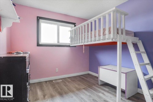 Spacious room with wood-finish flooring, a contemporary window with dark trim, light pink and purple painted walls, and white baseboards - 13224 37 Street, Edmonton, AB 
