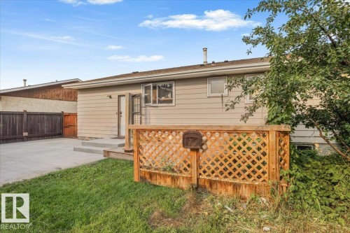 Rear exterior with light-colored siding, featuring a concrete patio and a wooden lattice fence - 13224 37 Street, Edmonton, AB 