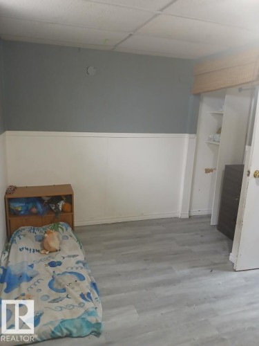 Room featuring light gray wood-finish flooring, two-tone wall paint with a white wainscoting-style lower section, and a drop ceiling - 13224 37 Street, Edmonton, AB 
