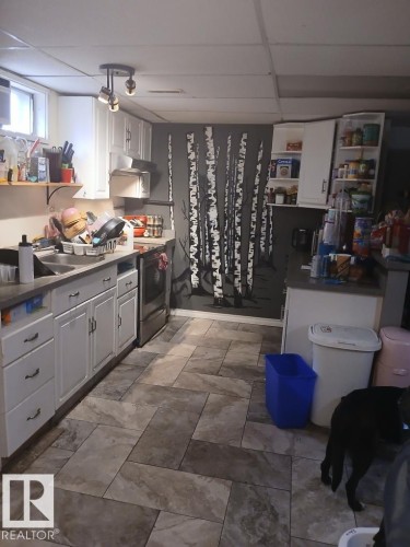 Kitchen featuring white cabinetry, track lighting, and a patterned accent wall - 13224 37 Street, Edmonton, AB 
