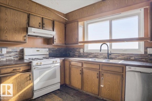 Kitchen featuring wood-finish cabinetry, tile backsplash, and a double-basin sink with a matte black faucet - 13224 37 Street, Edmonton, AB 