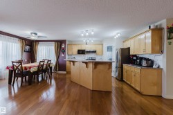 Open-concept kitchen and dining area featuring wood-finish flooring, light-toned cabinetry, an island with integrated seating, and stainless steel appliances - 