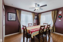 Dining area featuring wood-finish flooring, two large windows with sheer and opaque drapery, and a ceiling fan with integrated lighting - 