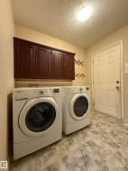 Dedicated laundry space featuring resilient flooring, overhead cabinetry, and recessed lighting - 