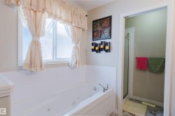 White jetted soaking tub with chrome fixtures, surrounded by white tile wainscoting - 