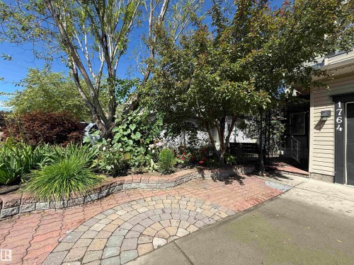 Landscaped front yard featuring mature trees and a curved paver patio - 1764 Melrose Crescent, Edmonton, AB 
