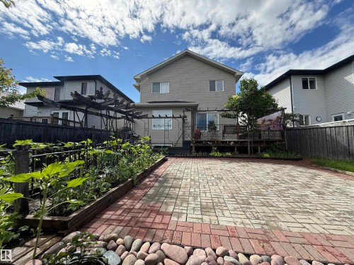 Expansive backyard featuring a large paved patio with a red brick border, raised garden beds with mature plants, and a wooden deck with a sliding glass door - 1764 Melrose Crescent, Edmonton, AB 