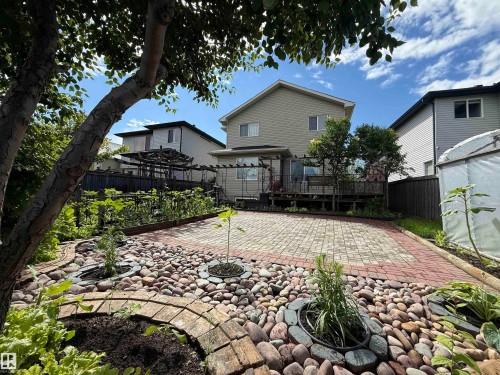 Spacious backyard featuring a large brick paver patio, decorative stone landscaping, mature trees, a multi-level wooden deck with pergola, and a garden bed - 1764 Melrose Crescent, Edmonton, AB 