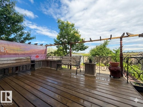 Spacious outdoor deck featuring wood-finish flooring, a decorative metal railing, a pergola structure, and mature perimeter trees - 1764 Melrose Crescent, Edmonton, AB 