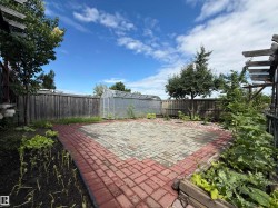Paved patio area featuring brick edging, perimeter fencing, a clear greenhouse structure, raised garden beds, and mature trees - 