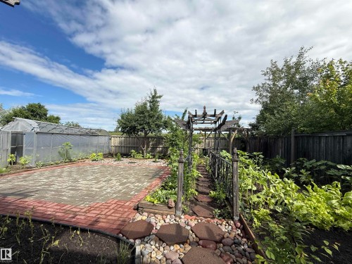 Expansive backyard featuring a large paved patio with red brick border, a spacious greenhouse structure, and a charming wooden pergola - 1764 Melrose Crescent, Edmonton, AB 