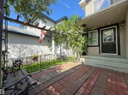 Brick paver patio with an overhead wooden pergola, leading to a dark paneled entry door with glass inserts and an exterior wall sconce - 