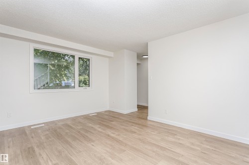 Open-concept room featuring light wood-finish flooring, white walls, and a large window with white trim - 5418 144B Avenue, Edmonton, AB 