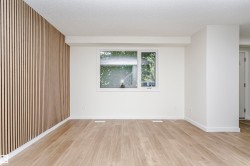 Spacious interior featuring a contemporary accent wall with vertical wood paneling, light wood-finish flooring, and a large window providing natural light - 