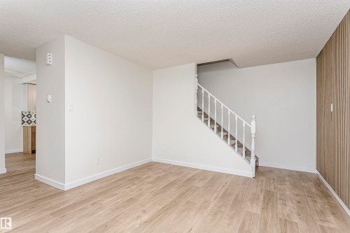 Open concept living area featuring light wood-finish flooring, white painted walls, a white staircase with balusters, and a textured accent wall - 5418 144B Avenue, Edmonton, AB 