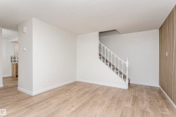 Open concept living area featuring light wood-finish flooring, white painted walls, a white staircase with balusters, and a textured accent wall - 
