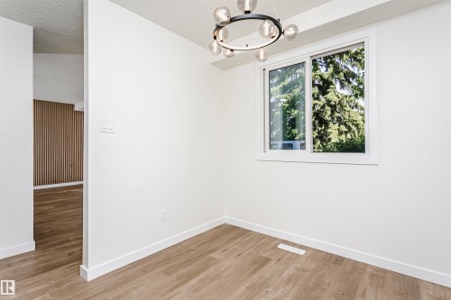 Room with light wood-finish flooring, white walls, and a modern circular chandelier - 5418 144B Avenue, Edmonton, AB 