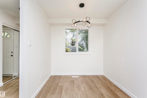 Light-filled interior space featuring a contemporary chandelier, a white-framed window, and wood-finish flooring - 5418 144B Avenue, Edmonton, AB 