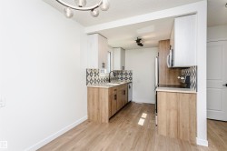 Kitchen featuring wood-finish flooring, two-tone cabinetry, a geometric tile backsplash, stainless steel appliances, and a modern ceiling light fixture - 