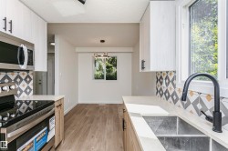 Modern kitchen featuring white cabinetry, light countertops, stainless steel appliances, a geometric tile backsplash, and wood-finish flooring - 