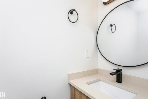 Bathroom vanity featuring a light-toned countertop, undermount sink, and matte black faucet - 5418 144B Avenue, Edmonton, AB 