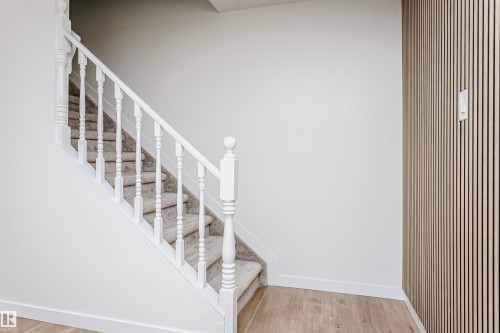 Staircase with white balusters and carpeted treads, complemented by light wood-finish flooring and a contemporary slat accent wall - 5418 144B Avenue, Edmonton, AB 