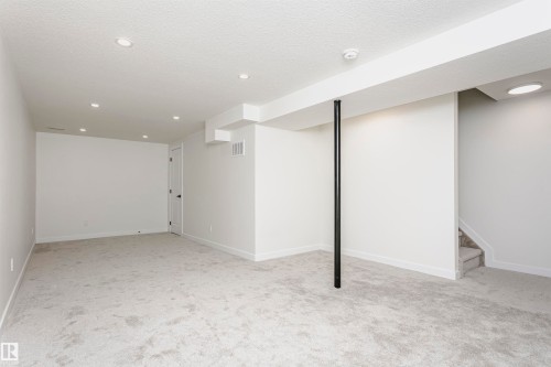 Spacious room featuring light-toned carpeting, recessed ceiling lighting, a white painted door with black hardware, and an exposed structural beam - 5418 144B Avenue, Edmonton, AB 