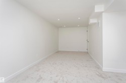 Spacious room featuring light gray carpeting, crisp white walls, recessed ceiling lighting, and a white door with black hardware - 