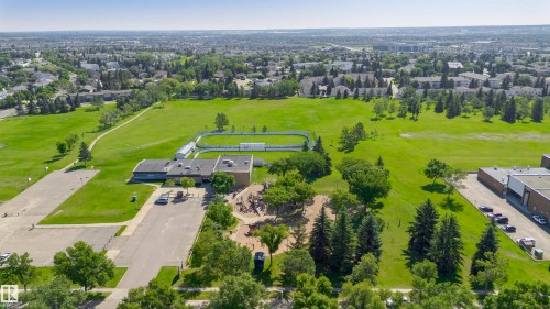 Expansive green space featuring large grass areas, mature trees, a paved parking lot, and a community building with a flat roof - 5418 144B Avenue, Edmonton, AB 