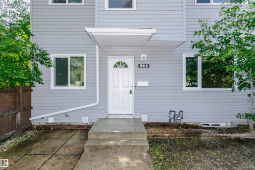 Light gray horizontal siding exterior with white trim windows and a white paneled entry door featuring an arched window detail - 5418 144B Avenue, Edmonton, AB 
