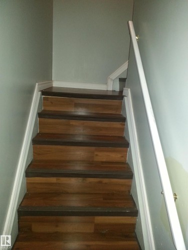 Staircase with wood-finish treads and risers, white trim, and a wall-mounted handrail - 8433 29 Avenue, Edmonton, AB - Indoor Photo Showing Other Room