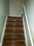 Staircase with wood-finish treads and risers, white trim, and a wall-mounted handrail - 