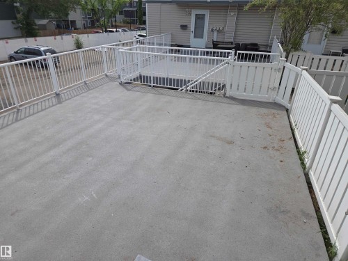 Expansive concrete patio area featuring white perimeter railings and a gated entry to a lower-level deck - 8433 29 Avenue, Edmonton, AB - Outdoor With Exterior