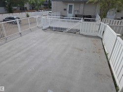 Expansive concrete patio area featuring white perimeter railings and a gated entry to a lower-level deck - 