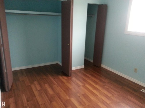 Room featuring wood-finish flooring, two bi-fold door closets with hanging rods, and a white-framed window - 8433 29 Avenue, Edmonton, AB - Indoor Photo Showing Other Room