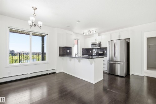 Open-concept kitchen and dining area featuring dark wood-finish flooring, white cabinetry, stainless steel appliances, and a central island with a sink - 435 5515 7 Avenue, Edmonton, AB 