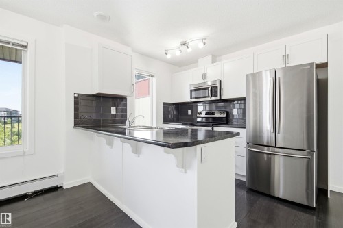 Modern kitchen featuring white cabinetry, dark wood-finish flooring, a black tile backsplash, and stainless steel appliances - 435 5515 7 Avenue, Edmonton, AB 