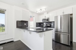 Modern kitchen featuring white cabinetry, dark wood-finish flooring, a black tile backsplash, and stainless steel appliances - 